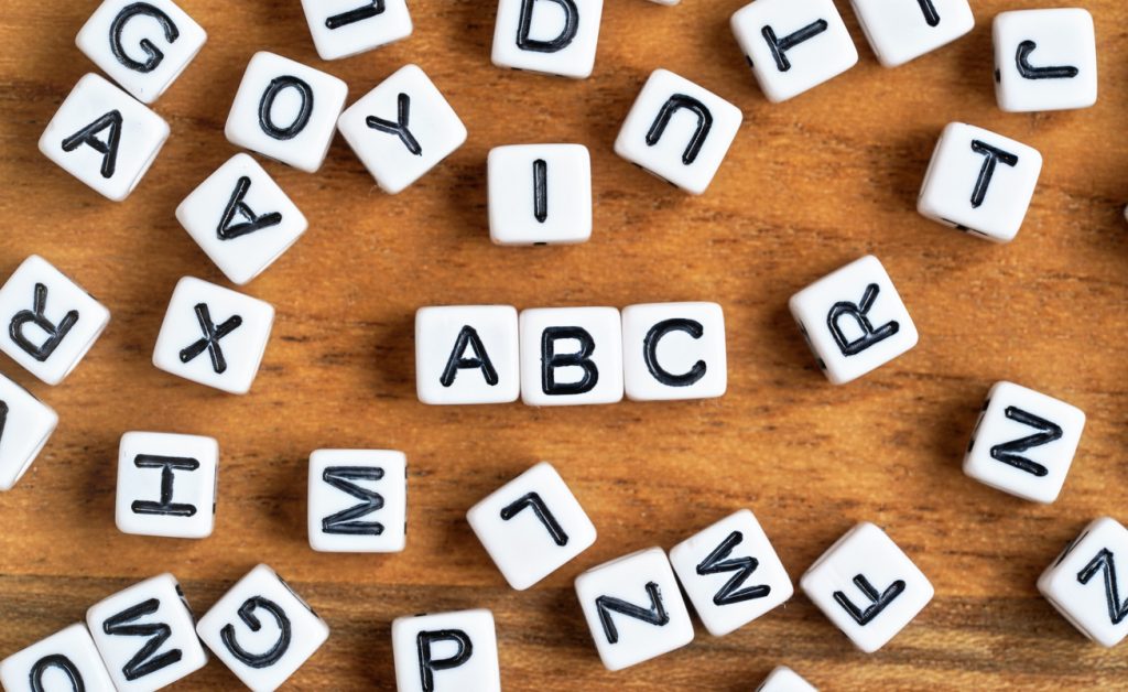 Small white and black bead cubes on wooden board, letters in middle spell ABC